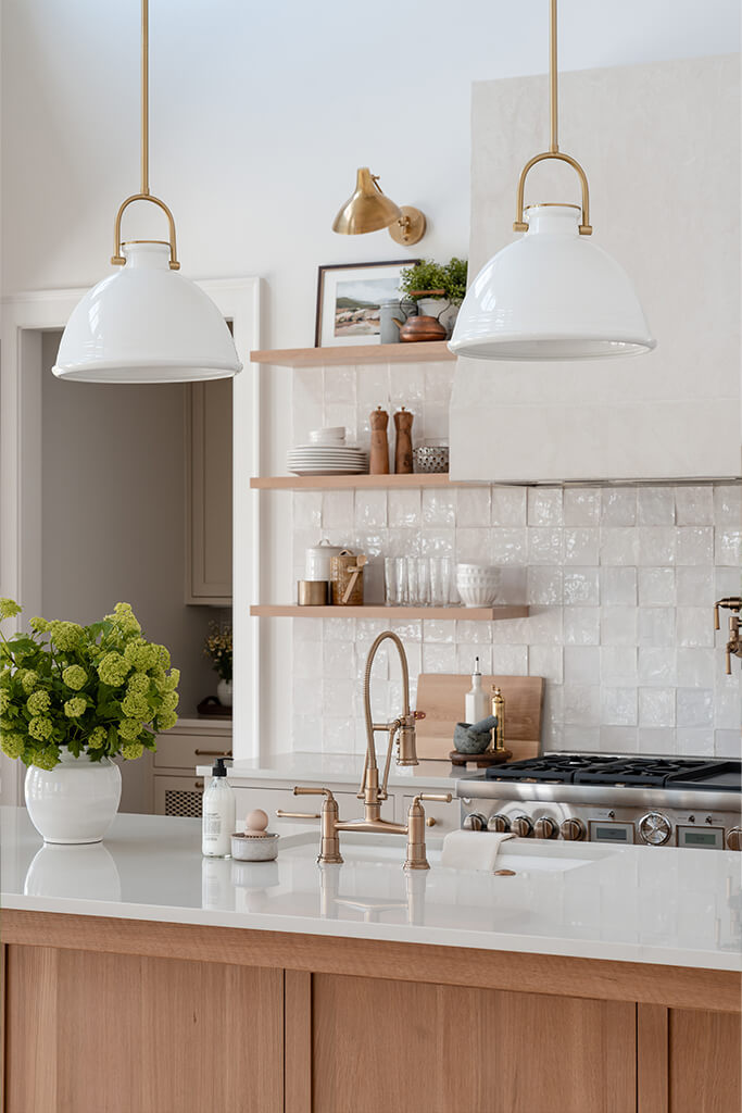 Detail image of a modern kitchen with hanging overhead lights, gold plated sink fitures, and marzipan terrazzo tile backsplash.